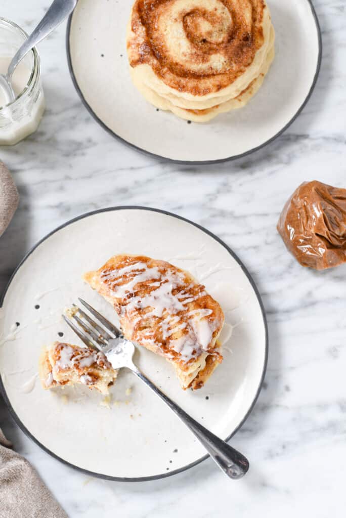 A fork with a bite of cinnamon roll pancake on a plate.