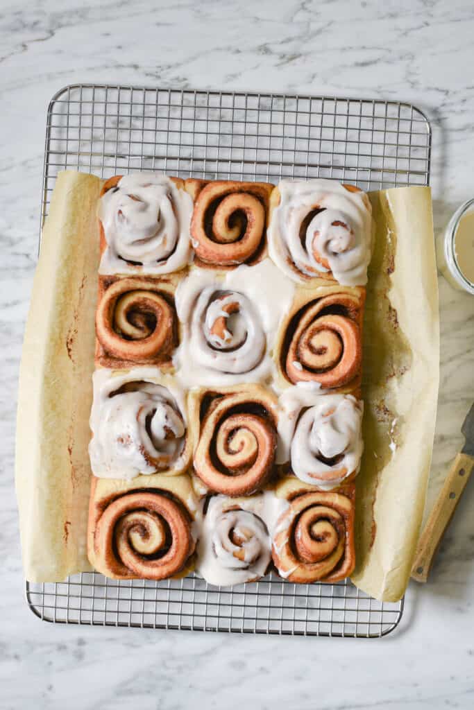 Vegan cinnamon rolls in a parchment sling on a wire rack to cool before icing.